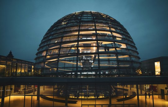 Die Kuppel des Reichstagsgebäudes hell erleuchtet bei Nacht in einer Seitenansicht. 